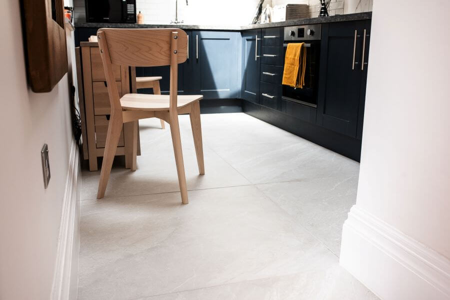 HAVEN-STONE-ANNEX. Image shows stone effect tile on floor of kitchen with blue cabinetry and light wood chair and table