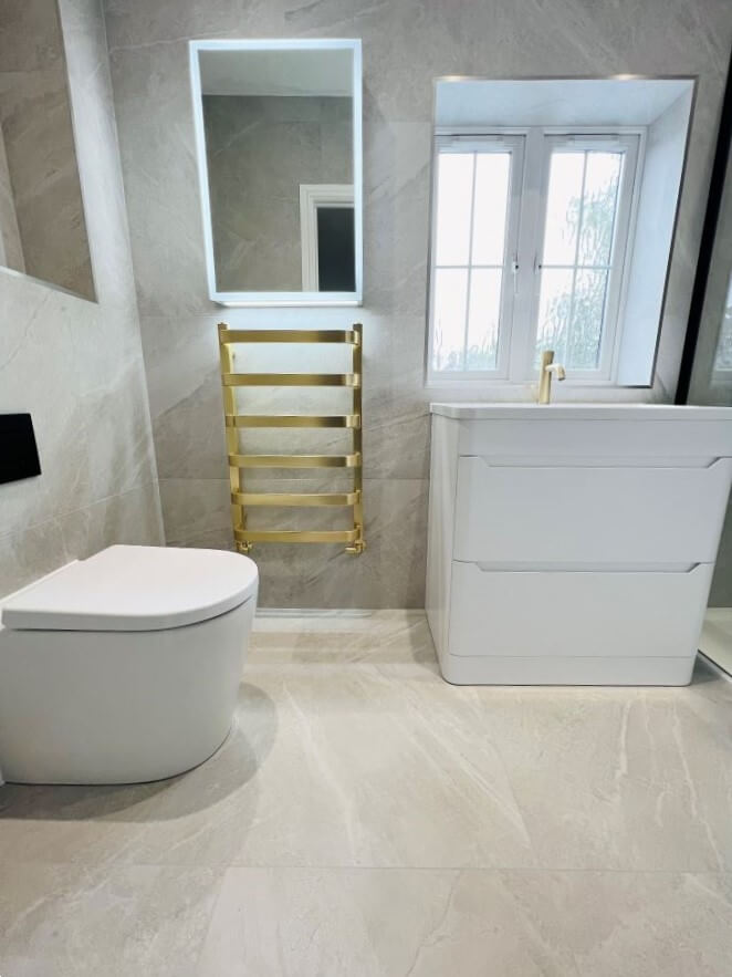 HAVEN-STONE. Image shows grey-brown tile with light white veining in bathroom with gold radiator and white sanitaryware