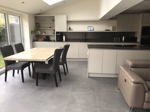 BLEND-PEAT-PORCELAIN-TILES. Image shows dark brown tiles in lounge with sofa and a kitchen in the background