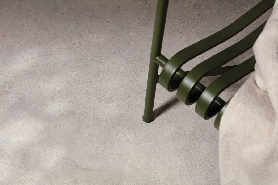 CHIC-LIMESTONE-PORCELAIN-FLOOR-TILE-1. Image shows limestone porcelain floor tile with green chair and towel