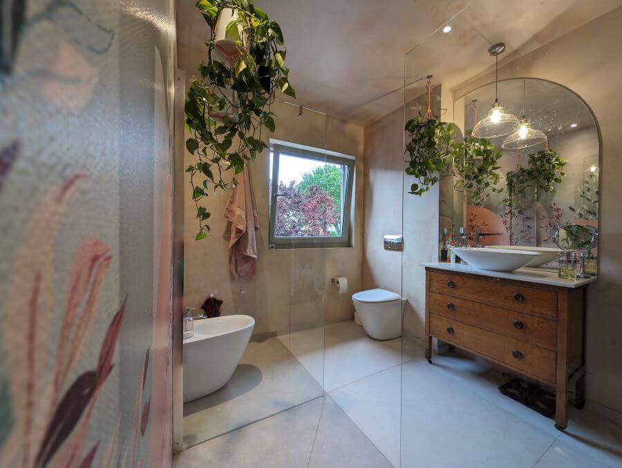 A-ROOM-IN-THE-GARDEN. Image shows cream and beige tiles to floor with wooden vanity unit and sink and large mirror