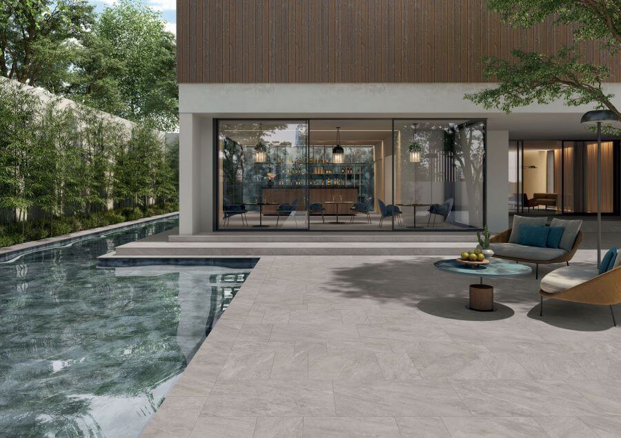 ALPINE-SEPIA-QUARTZ-EFFECT-PORCELAIN-TILE. Image shows light grey quartz effect porcelain tile around a swimming pool with outdoor furniture