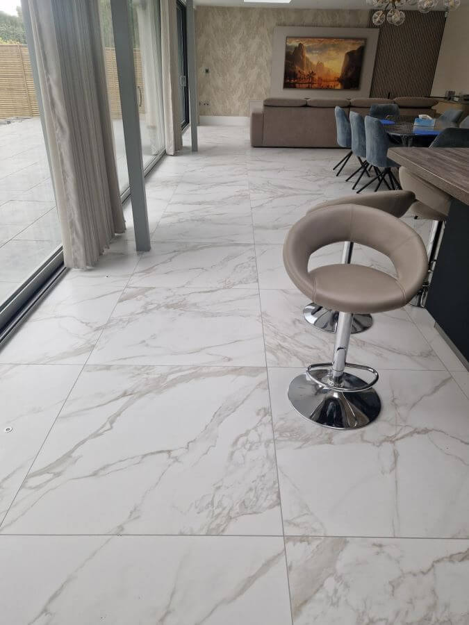 CARERRA-ORO-MARBLE-TILE. Image shows gold veined marble porcelain tile in lounge with table and chairs near window