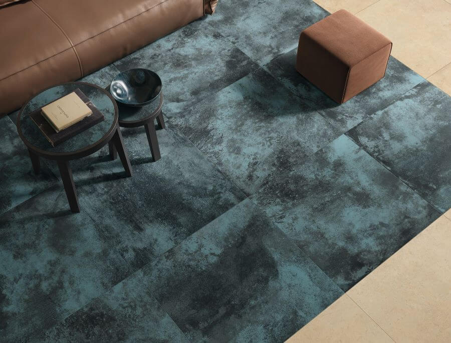 FORGE-BLUE-MOTTLE-PORCELAIN-METALLIC-TILES-FLOOR-CLOSEUP. Image shows blue metallic tiles to floor of lounge with brown sofa and a table