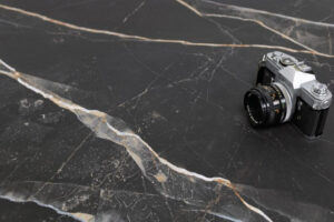 MARQUINA-ORO-MATT-MARBLE-EFFECT-PORCELAIN-TILE. Image shows matt black marble tile with gold and grey veins with camera