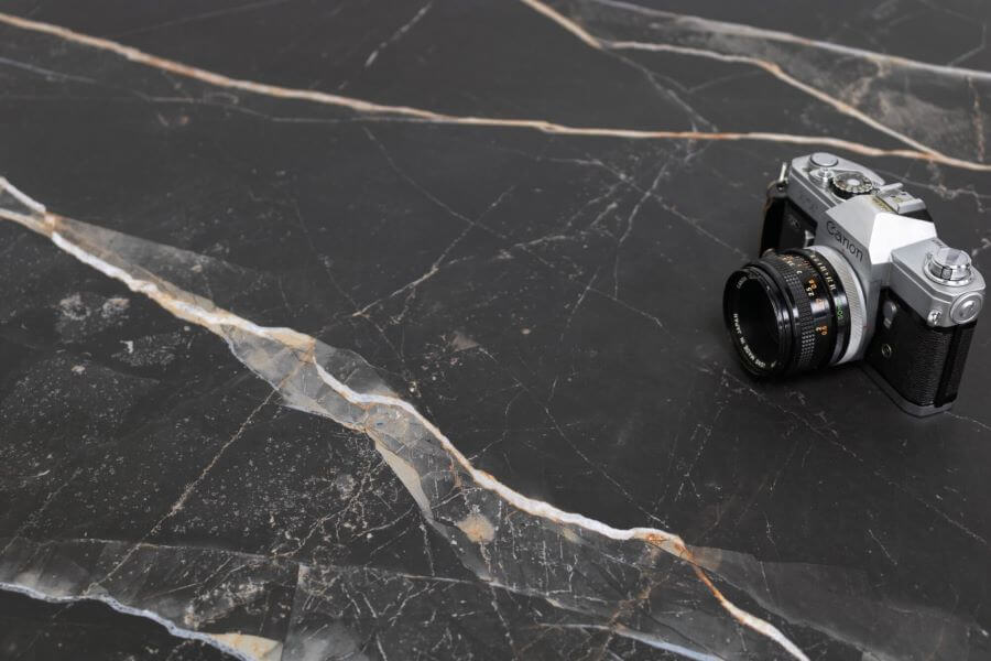 MARQUINA-ORO-MATT-MARBLE-EFFECT-PORCELAIN-TILE. Image shows matt black marble tile with gold and grey veins with camera