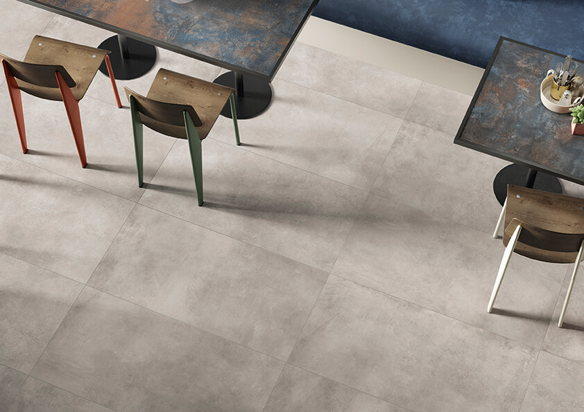 STRIDE-FORM-LARGE-FORMAT-CONCRETE-LOOK-PORCELAIN-TILE. Image shows light grey concrete look porcelain tile in restaurant with tables and chairs