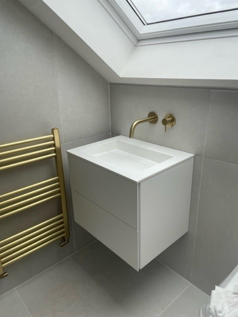 ABODE-WHITE. Image shows white wall and floor tiles with brushed gold radiator and a white sink unit