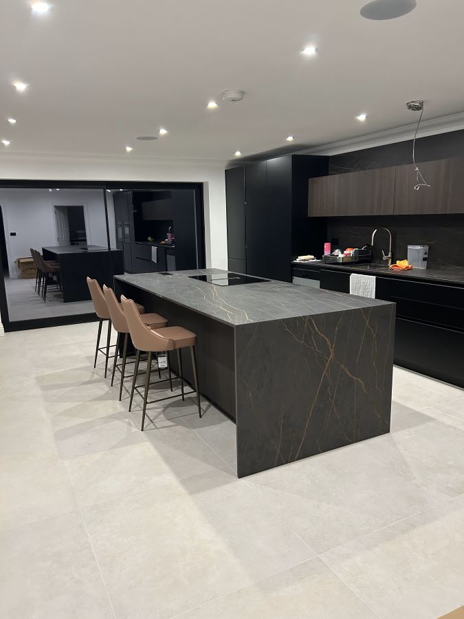 METRO-BONE-KITCHEN. Image shows cream tile in kitchen with black and gold island unit in centre and kitchen to the right